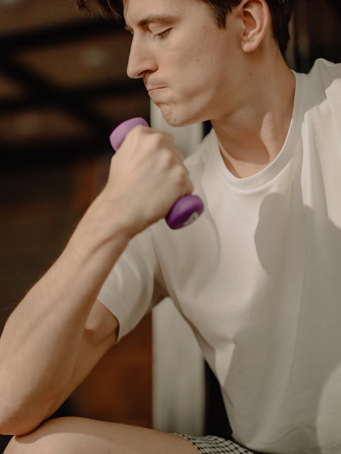 Focused young man lifting a dumbbell at home. Achieving fitness goals indoors.